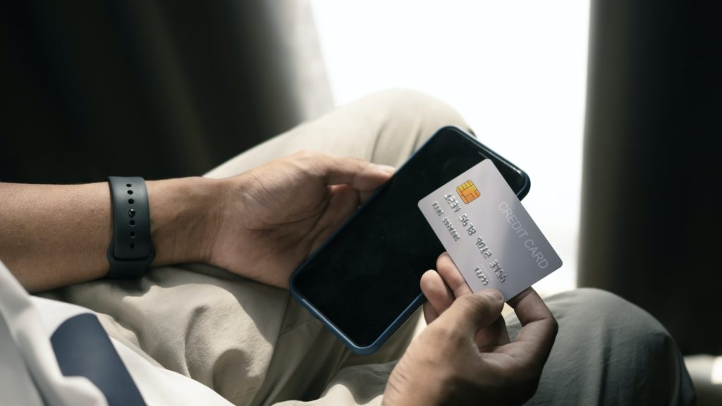 Close up view of man holding credit card and using smart phone for online payment.